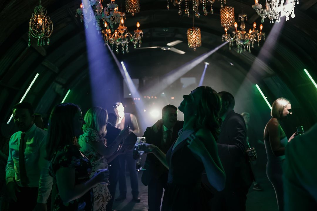 Guests dancing beneath chandeliers and beams of light